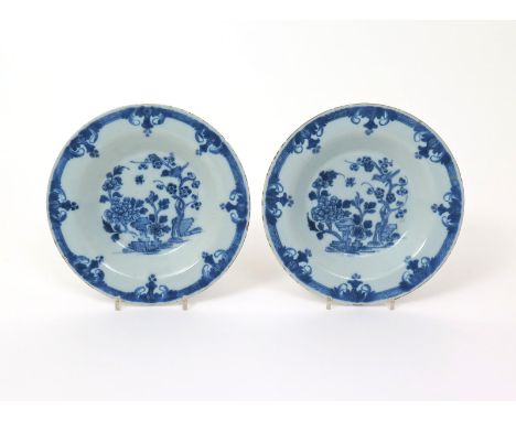 A pair of Dublin delftware soup plates, c.1760, each painted in blue with a bird perched in a prunus tree beside flowering pe