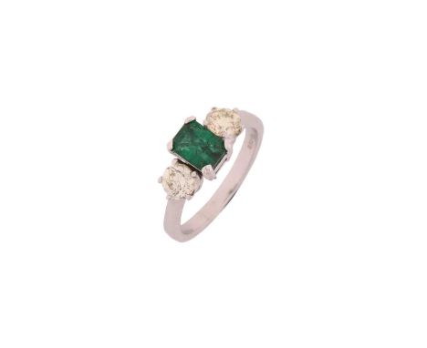 A diamond and emerald three stone ring, comprises an emerald-cut emerald measuring 6.6 x 5.0 mm, with deep green body colour,