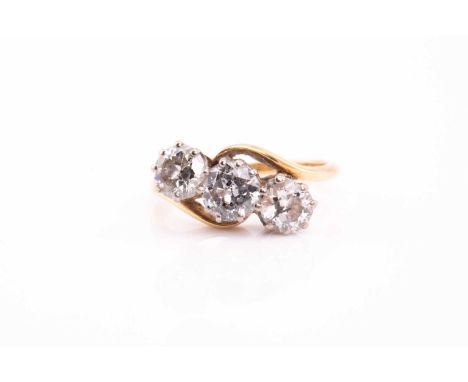 A three stone diamond crossover ring; the slightly graduated round brilliant cut diamonds in claw set crossover mount and pla