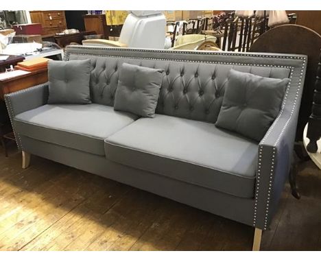 A stylish modern three seater sofa upholstered in grey linen with button upholstered back and steel studded detail, complete 