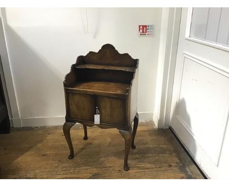 A figured walnut bedside with scalloped top and open shelf above two panel doors, raised on carved moulded supports and pad f