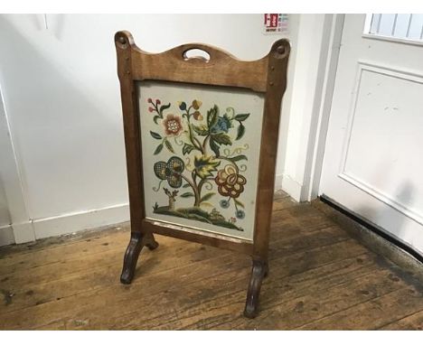 An Arts &amp; Crafts oak firescreen with arched centre handle to top enclosing a glazed crewel work style floral deer and rab