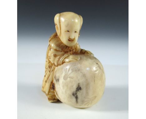 A late 19th/early 20th century marine ivory netsuke stained and carved as a boy standing over a giant peach, signed in black,