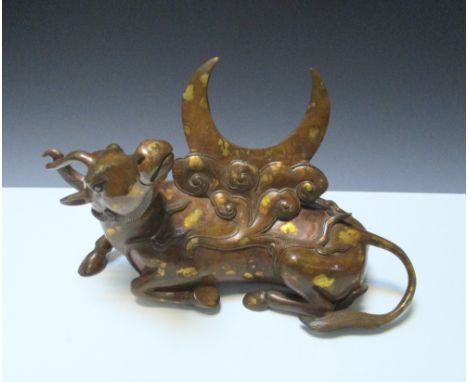 A gold splashed bronze qilin, the single horned reclining animal looking up towards the crescent backed stand on its back, 26