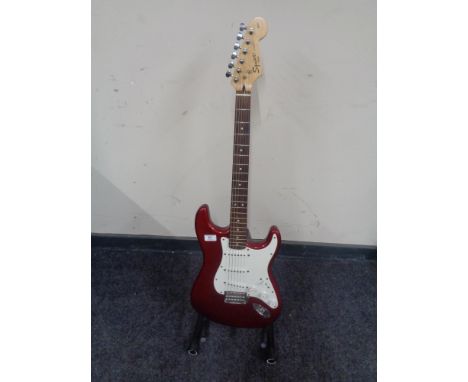 A Squier by Fender Strat electric guitar, red, together with a folding guitar stand. (2)