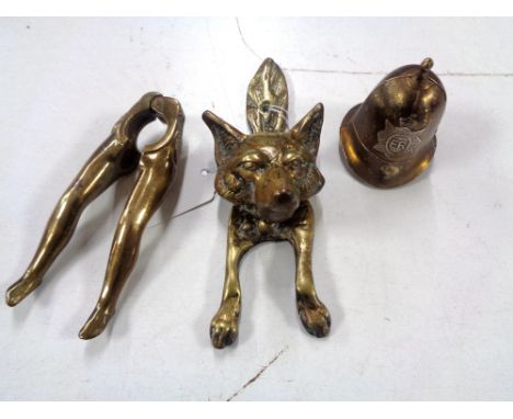 A Victorian brass fox door knocker, together with brass 'legs' nut cracker and Police helmet table bell. (3)