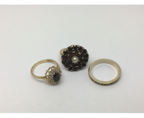 An eternity ring, a ring set with garnets and a central pearl plus a cz ring set with a central blue stone (3). Approx total 