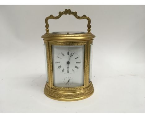 A French engraved gilt brass oval carriage clock with push button repeat and alarm the dial with Roman numerals and second su