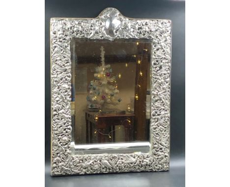 AN ANTIQUE VICTORIAN HALLMARKED SILVER FRONTED EASEL BACKED MIRROR WITH A CHASED AND PIERCED FOLIATE,BIRD AND CHERUB BORDER. 