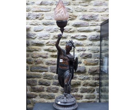 A SPELTER FIGURAL LAMP CAST AS AN AMERICAN INDIAN WITH BOW AND SHIELD IN HIS LEFT HAND WHILE THE LAMP IS HELD UP IN HIS RIGHT