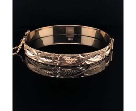 A 9ct GOLD HALLMARKED HINGED BANGLE, WITH DIAMOND CUT DESIGN TO ONE HALF, COMPLETE WITH SAFETY CHAIN. WEIGHT 15grms. 