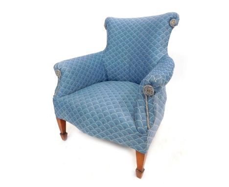 An early 20thC low seated upholstered armchair, with blue scale pattern upholstery, on square tapered legs and spade feet.