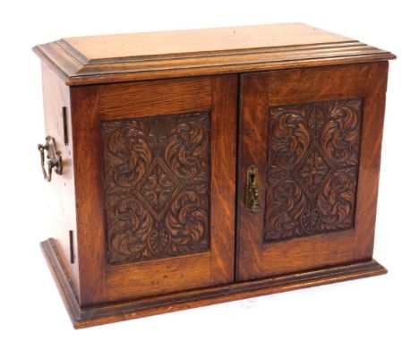 A 19thC oak smoker's cabinet, with carved panelled doors and a fitted interior with tobacco jar and two drawers, with brass s