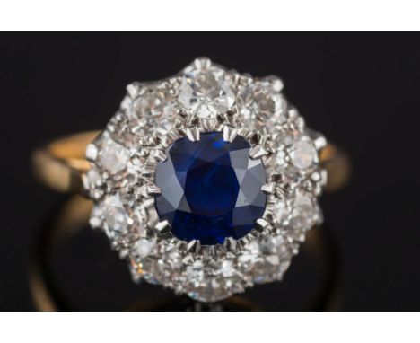 A sapphire and diamond circular cluster ring: with central round sapphire approximately 1.3cts claw-set within a surround of 