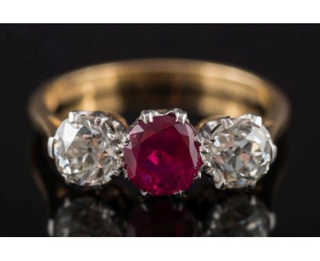 An 18ct gold, ruby and diamond three-stone ring: with central round ruby approximately 0.90ct between round old brilliant-cut