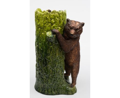 A Bretby pottery stick stand: modelled as a bear cub with inset glass eyes climbing a tree trunk, early 20th century, 67 cm h