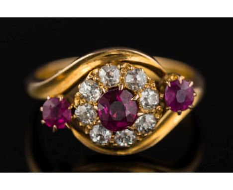 A late Victorian 18ct gold, ruby and diamond mounted circular cluster cross-over ring: the central oval ruby approximately 0.