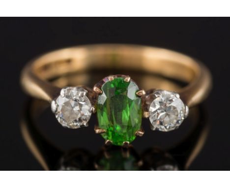 A demantoid garnet and diamond three stone ring: the central oval demantoid garnet approximately 6mm long x 4mm wide, between