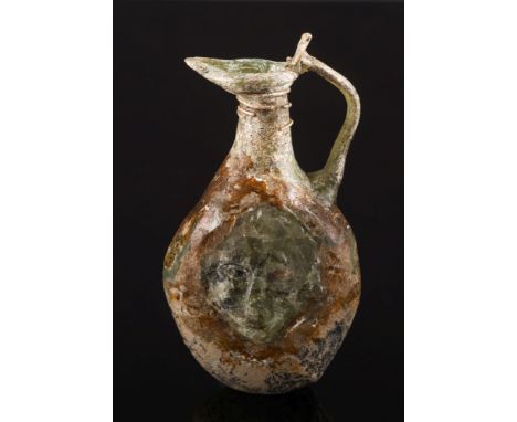 A Roman mould-blown olive green glass flask: of flattened form with a mask head to each side and simple loop handle, 1st-2nd 