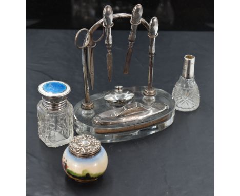 A 1930's silver and glass table top manicure set, the oval clear glass platform with recessed apertures and arched stand with