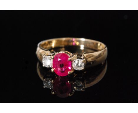 A modern 14ct ruby and diamond three stone ring, central oval ruby flanked by a brilliant cut diamond to each shoulder, all s