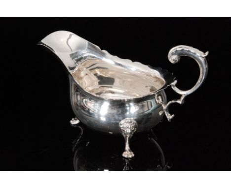 An Edwardian hallmarked silver sauce boat with cut edge rim and acanthus leaf capped flying scroll handle, raised on three li