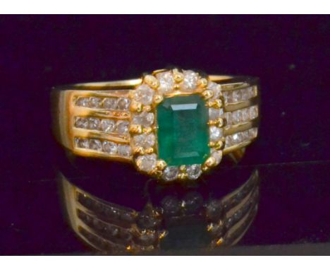 An emerald and diamond dress ring, the central step cut emerald claw set within a border of twelve brilliant cut diamonds, sh