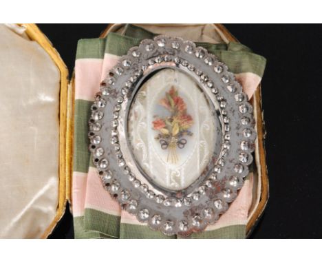 An 18th Century cut steel oval buckle with central spray of dried flowers to a white painted mirror base under glass panel to