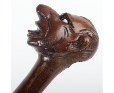 A carved wood ‘grotesque’ walking stick, the handle carved with stylised head, protruding nose and mouth agape, 92cm