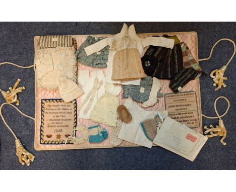 A mid 19th Century embroidered presentation folio with 4 tassels enclosing an offering of embroidered and hand sewn dolls clo