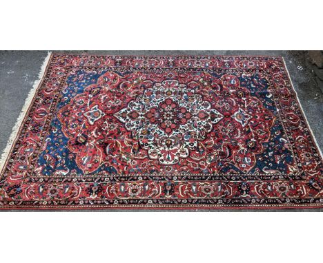A Persian handwoven Heriz rug, having a central medallion on a red ground with floral motifs, the surrounding multi-guard bor