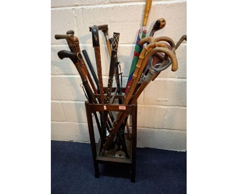 A quantity of vintage walking sticks, shooting sticks, an umbrella and an umbrella frame all housed in an oak stick/umbrella 