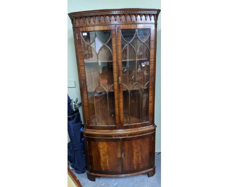 A reproduction mahogany bow fronted corner cabinet, dentil moulded cornice with arched moulded decoration, above astragal gla