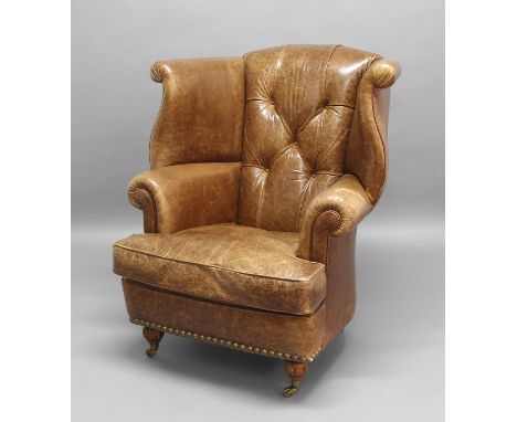 LEATHER BUTTON BACK WING ARMCHAIR, with scrolling wings above outswept arms, on squat reeded legs and brass castors, height 1