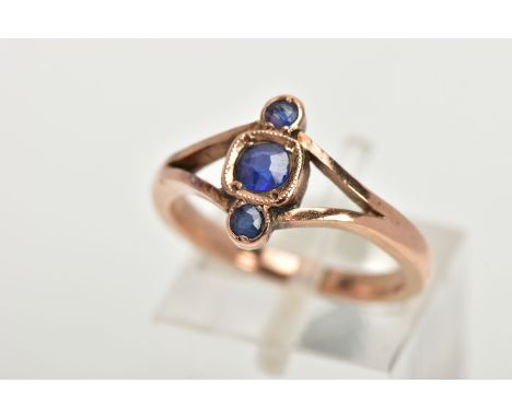 A THREE STONE RING, three graduated circular cut blue stones, within a rose gold tone mount, bifurcated shoulders leading ont