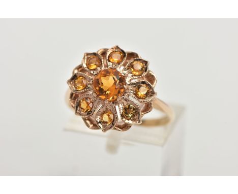 A 9CT GOLD CLUSTER RING, in the form of a flower, set with a central circular cut orange stone assessed as citrine within a p