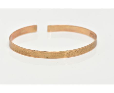 A YELLOW METAL TORQUE BANGLE, engine turned design, personal engraving to the interior of the bangle reads 'Jacquelines 1st B