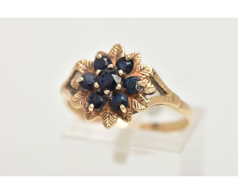 A 9CT GOLD SAPPHIRE CLUSTER RING, of a flower form, set with seven circular cut deep blue sapphires, within a textured leaf s