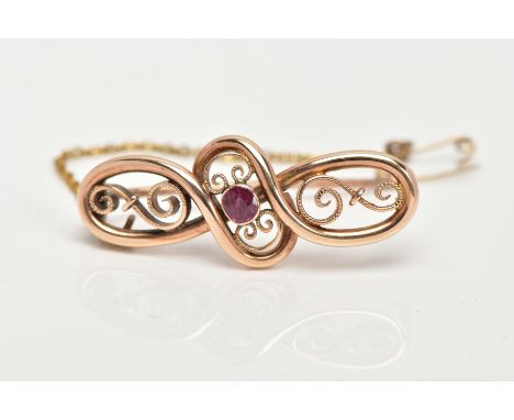 A VICTORIAN GOLD BROOCH, scrolled open work detailing with a central bezel set circular cut ruby, approximate length 37mm, fi