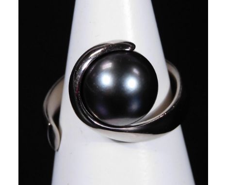 A Paul Spurgeon 18ct white gold and cultured pearl ring, designed as a ribbon of gold curled around a dark bluey/grey culture