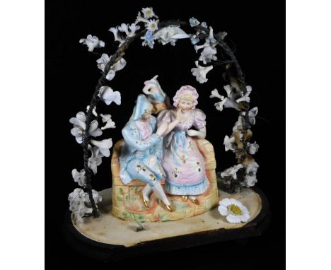 A late 19thC bisque figure group, on ebonised stand, formed as a lady and gentleman courting couple, in an arched floral entw