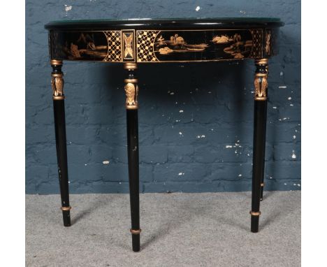 A black and gold lacquered semi-circular console table on reeded style legs. Comes with a glass top cover and decorated in an