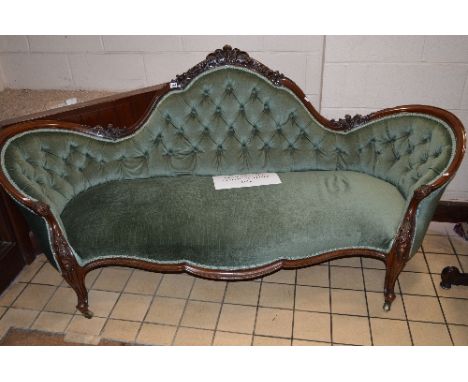 A VICTORIAN CARVED WALNUT GREEN UPHOLSTERED BUTTONED SOFA, with carved top rail, arched back to scrolled arms and legs on bra
