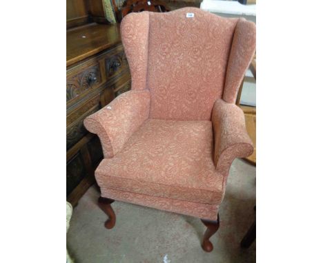 A vintage Parker Knoll wingback armchair with pink tapestry upholstery, set on cabriole front legs with pad feet - with fire 