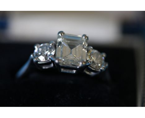 An 18ct white gold ring set with a central emerald cut diamond, approx. 1.75ct and flanked by two round cut diamonds, 0.5ct, 