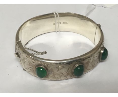 A wide bright cut silver bangle set with green stone cabochons.