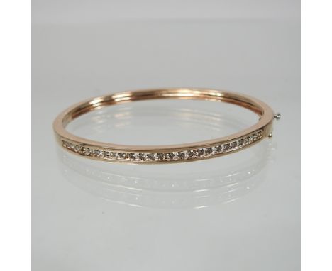 A 9 carat gold and diamond bangle, of hinged design, set with a single row of twenty-five channel set diamonds, 6.5cm wide