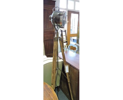 An industrial style floor lamp with brassed metal shade on adjustable wood tripod.