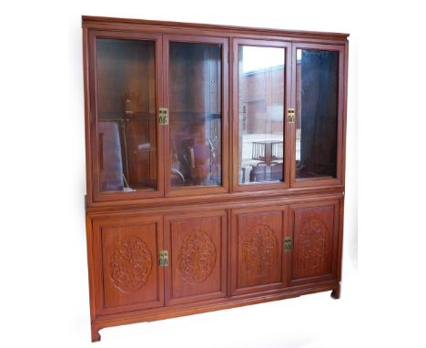 An oriental hardwood display cabinet, with a moulded cornice above four glazed doors, enclosing adjustable shelves, the base 