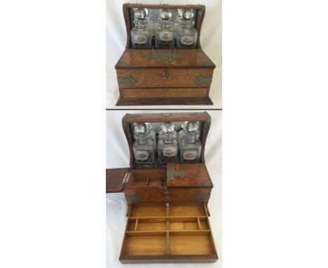 A Victorian oak cased triple decanter tantalus with lockable cabinet and mirrored back. With 3 cut glass decanters and silver